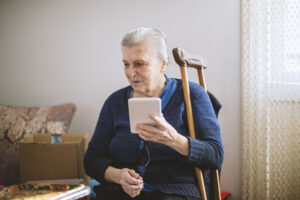 An older woman is seated in her home and talking on the phone.