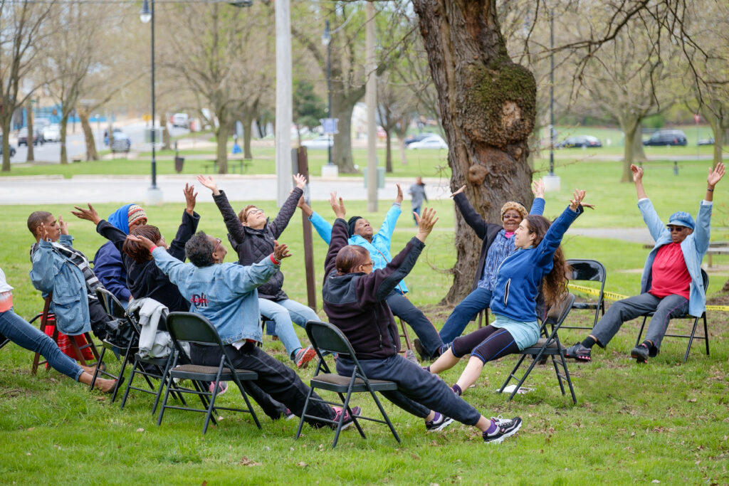 GrandFamily Resource Center participants do chair yoga in the park.