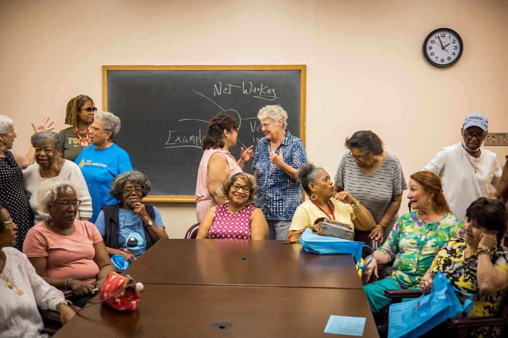 A group of older women are gathered for a Healthy Lives Group at Southwest Senior Center, talking and laughing together.