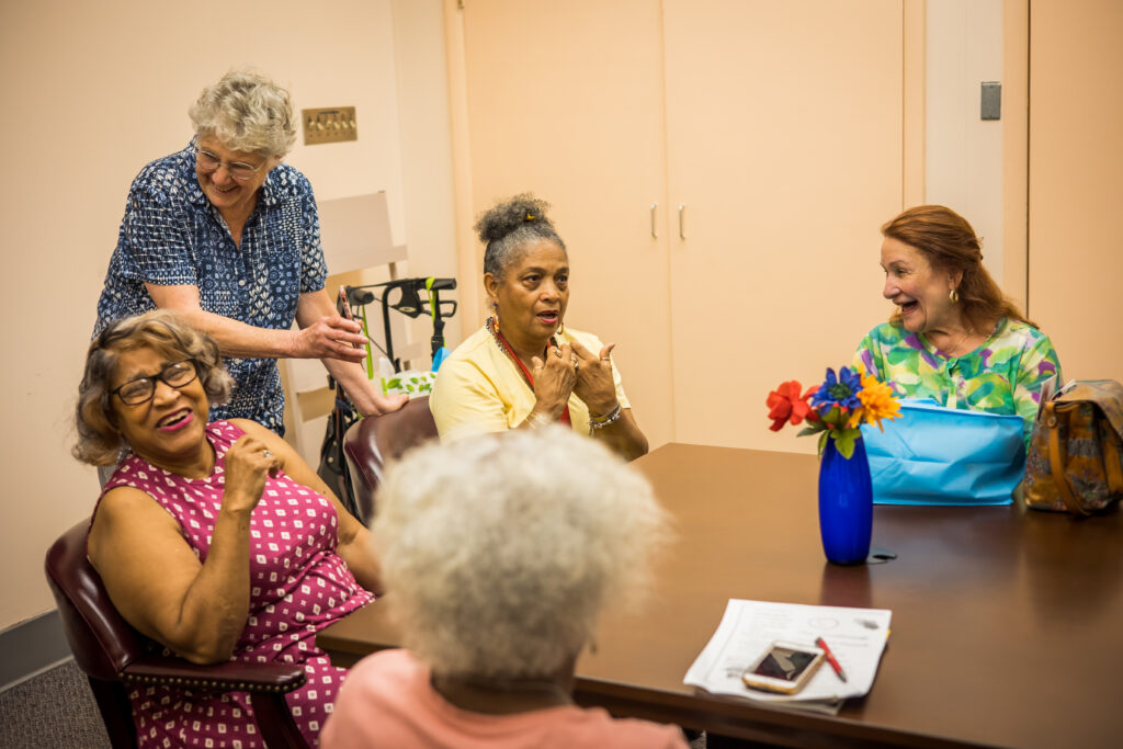 A group of older women are meeting at a Healthy Lives Community Group and laughing together